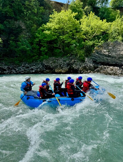 A group of people in a blue raft navigating a river surrounded by greenery. 2