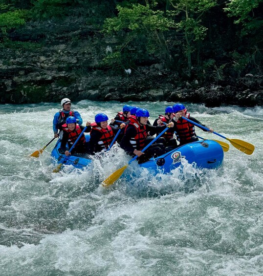 A group of people in a blue raft navigating a river with rapids. 1