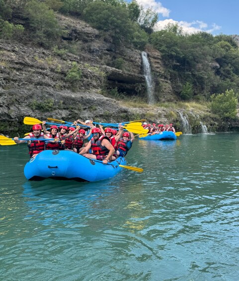 A group of people rafting on a river, surrounded by lush greenery and a waterfall. 3
