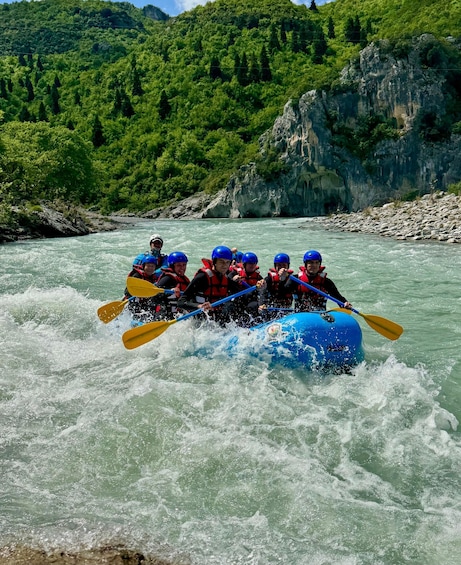 A group of people in a blue raft navigating a river with rapids, surrounded by lush green hills. 5