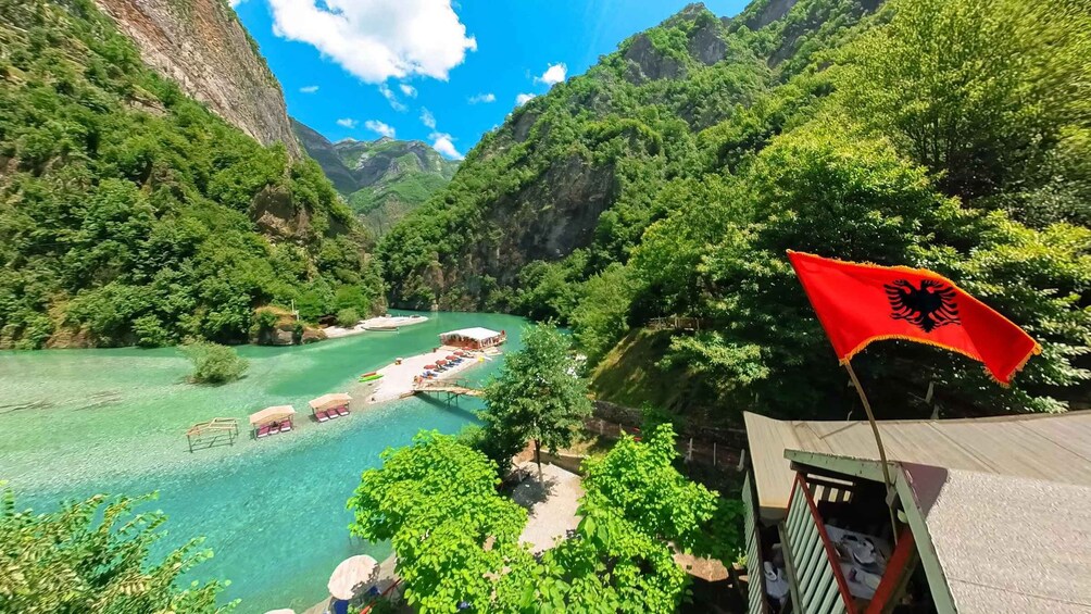 A river with clear water, surrounded by lush green mountains and a red flag with a black emblem. 3