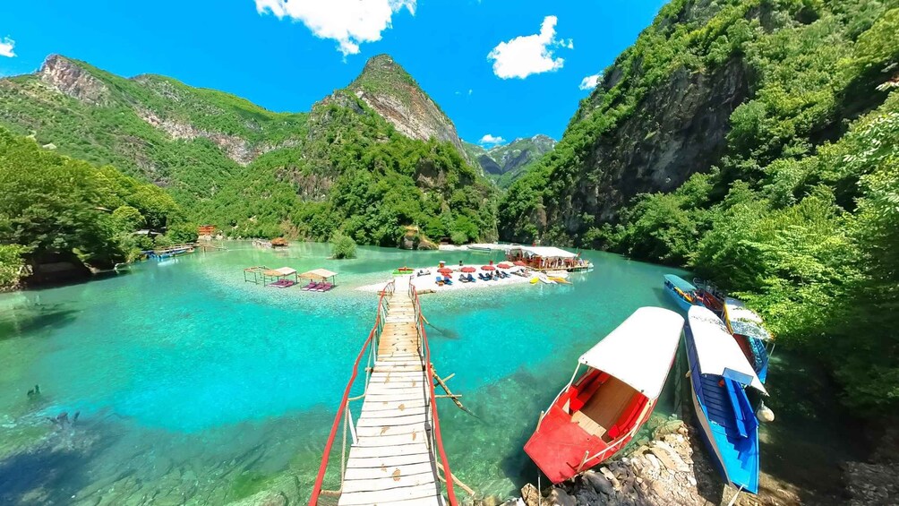 A wooden pier leading into a turquoise river surrounded by lush green mountains. 1