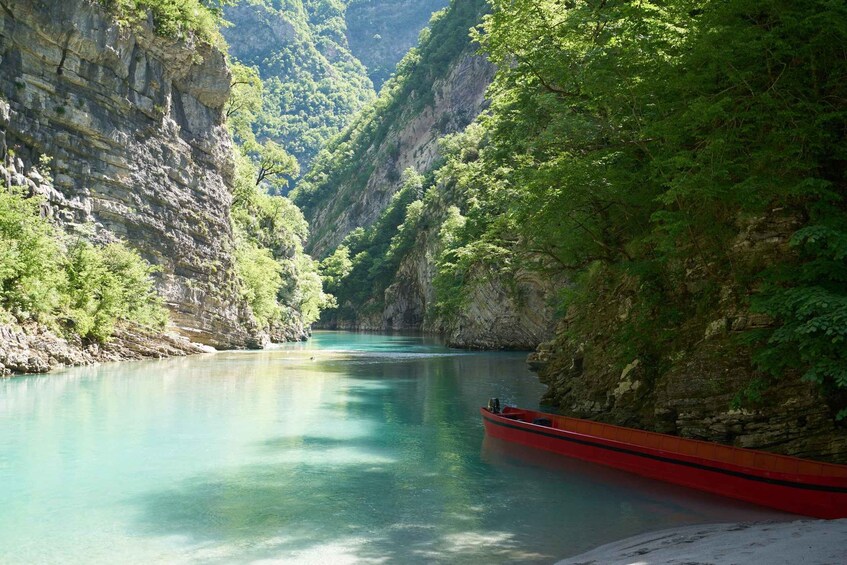A red canoe on a calm river surrounded by steep cliffs and lush greenery. 2
