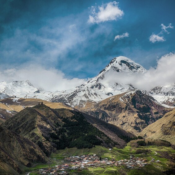 A snow-capped mountain, a valley with a small settlement, and a clear blue sky. 2