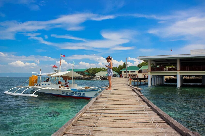 A wooden pier extending into clear turquoise waters with a boat named 'ZAJHON-DAVID' docked at the end. 5