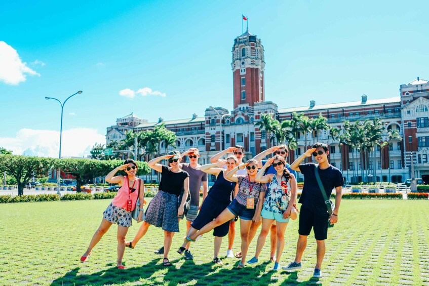 A group of people posing in front of a large building with a clock tower. 1