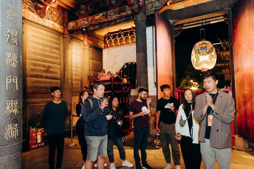 A group of people standing in front of a traditional building with ornate decorations and a hanging lantern. 5