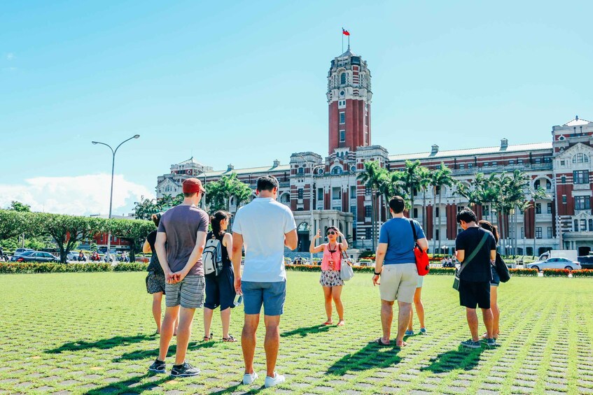 A group of people standing on a paved area with a large building featuring a clock tower in the background. 4