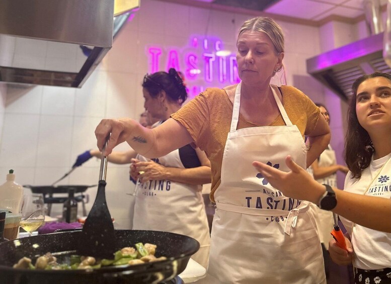 A cooking class with participants wearing aprons, one stirring a pan with food. 1