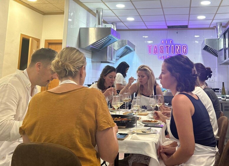 A group of people dining at a restaurant with a neon sign that reads 'ALC TASTING.' 3