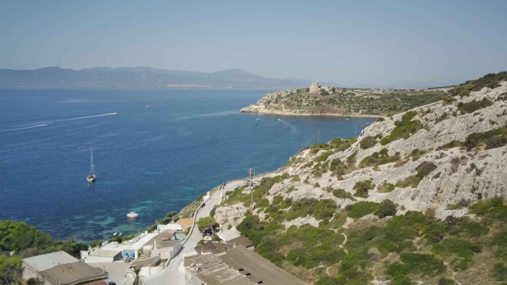 A coastal landscape with a rocky hill, clear blue sea, boats, and a lighthouse. 3