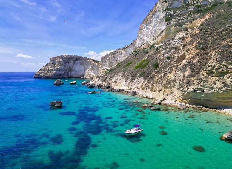 A coastal landscape with clear turquoise waters, rocky cliffs, and a boat. 1