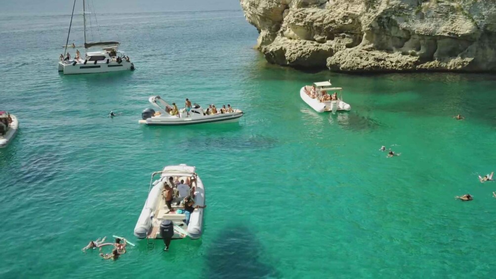 A group of boats on turquoise water near a rocky coastline. 4