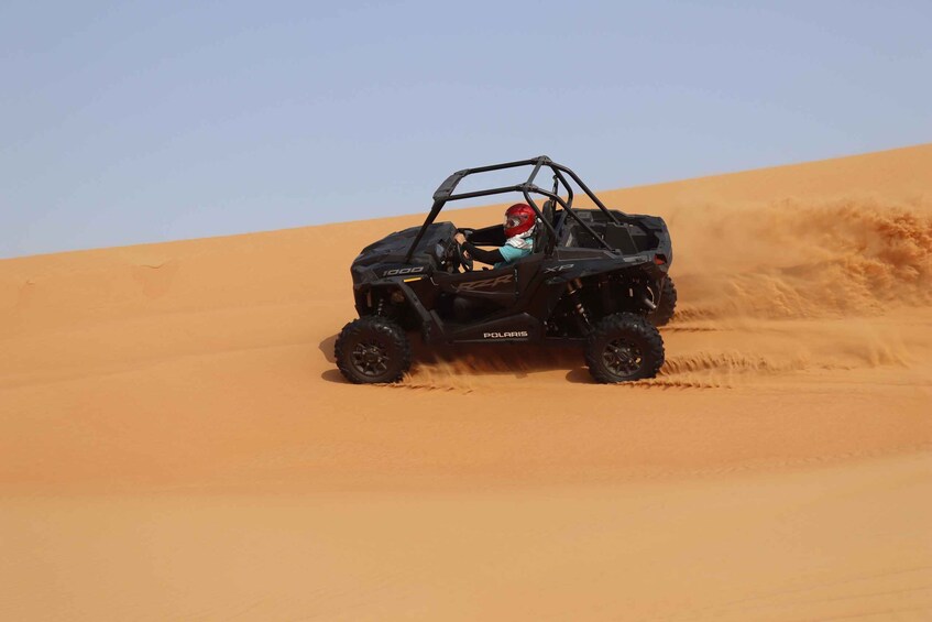 A Polaris off-road vehicle driving through a desert with sand dunes. 5