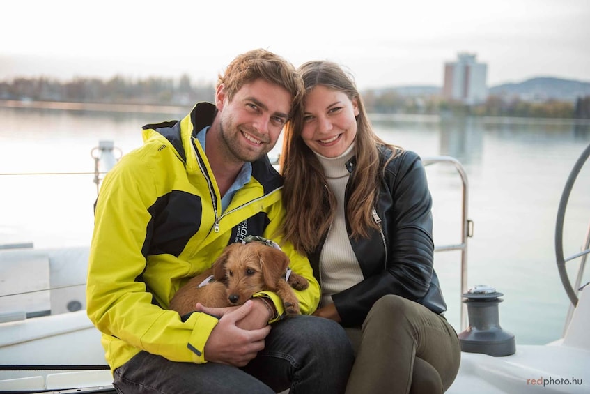 A couple on a boat with a dog, water in the background, and a city skyline. 4