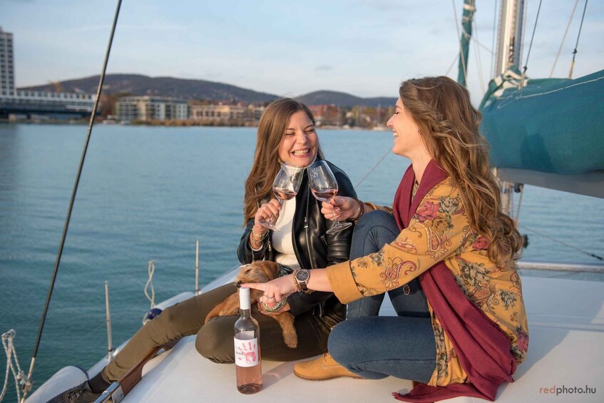 Two people sitting on a boat, holding wine glasses, with a bottle of wine on the deck. 1