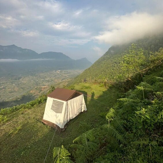 A tent on a grassy hillside with a mountainous landscape in the background. 1