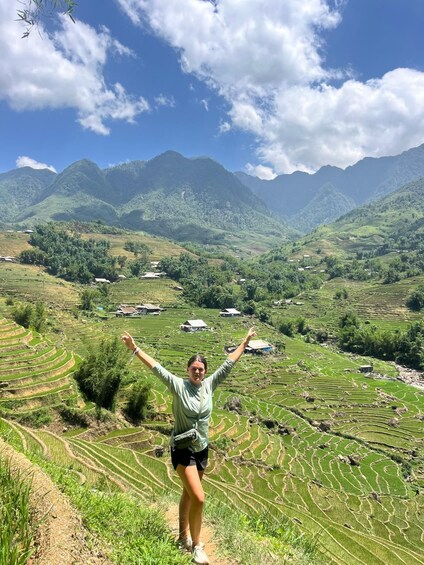 A person standing on a hillside with terraced fields and mountains in the background. 2