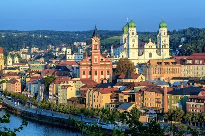 A cityscape with a prominent church with green domes, a river, and colorful buildings. 1