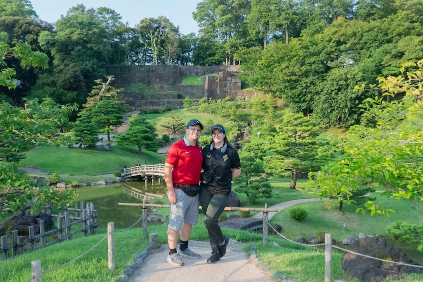 A couple standing on a path with a pond and a stone wall in the background. 2
