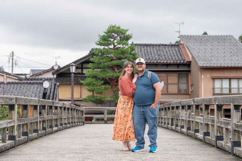 A couple standing on a bridge with traditional Japanese architecture in the background. 1