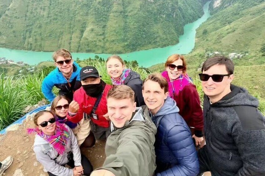 A group of people taking a selfie with a mountainous landscape and a turquoise river in the background. 4