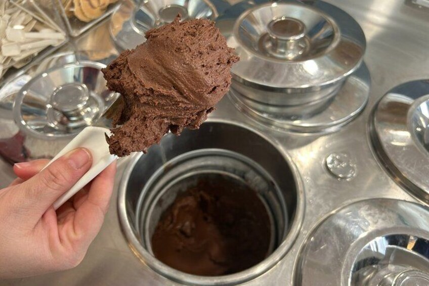 A hand holding a scoop of chocolate ice cream with a metal bowl in the background. 4