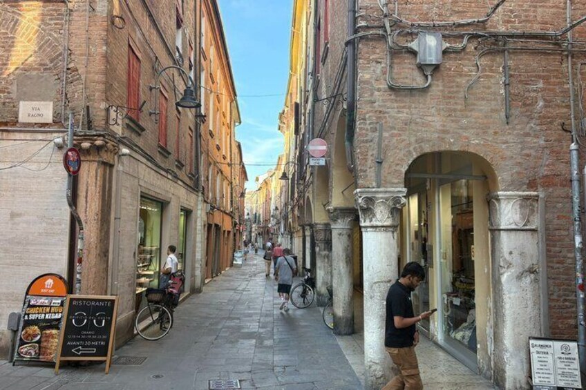 A narrow street with buildings, a signboard, and a person using a mobile phone. 5