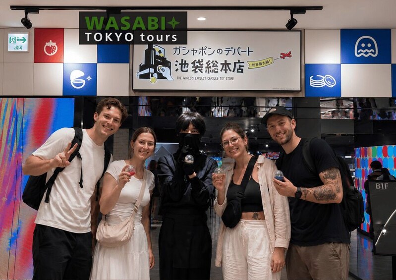 A group of people posing in front of a store with a sign that reads 'WASABI TOKYO tours' and 'THE WORLD'S LARGEST CAPSULE TOY STORE'. 1