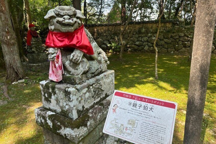 A stone lion statue with a red cloth, surrounded by trees and a stone wall. 4