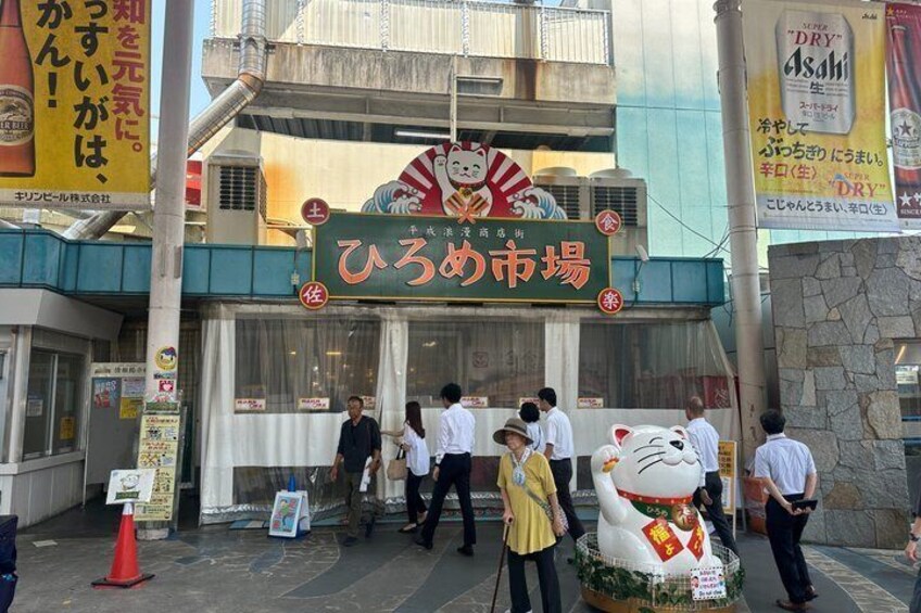 A street scene with a large cat statue, people walking, and a building with a sign. 2