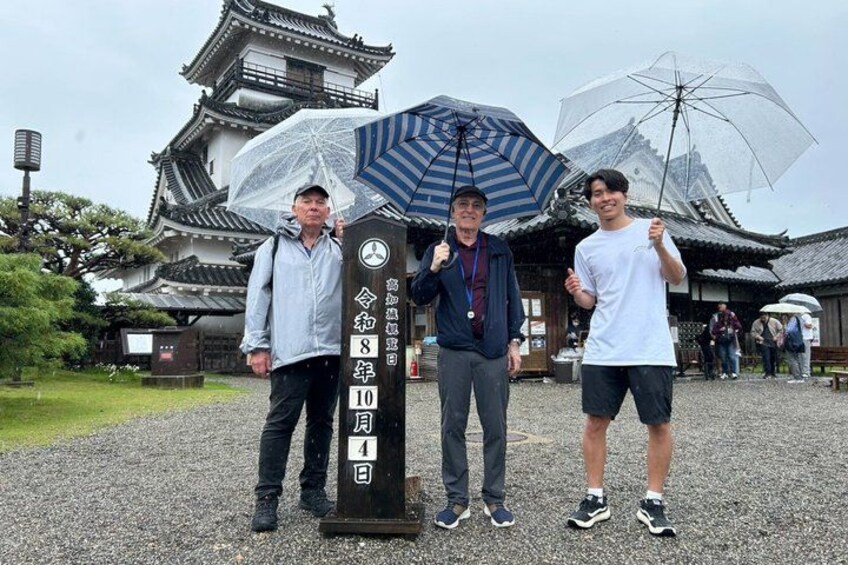 Three people standing in front of a traditional Japanese building with a signpost. 2