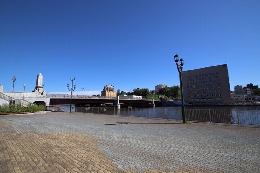 A riverside walkway with a bridge, a monument, and a modern building. 5