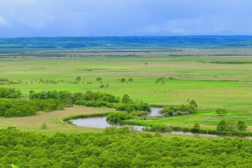 A vast green landscape with a river meandering through it, surrounded by dense greenery and distant hills. 4