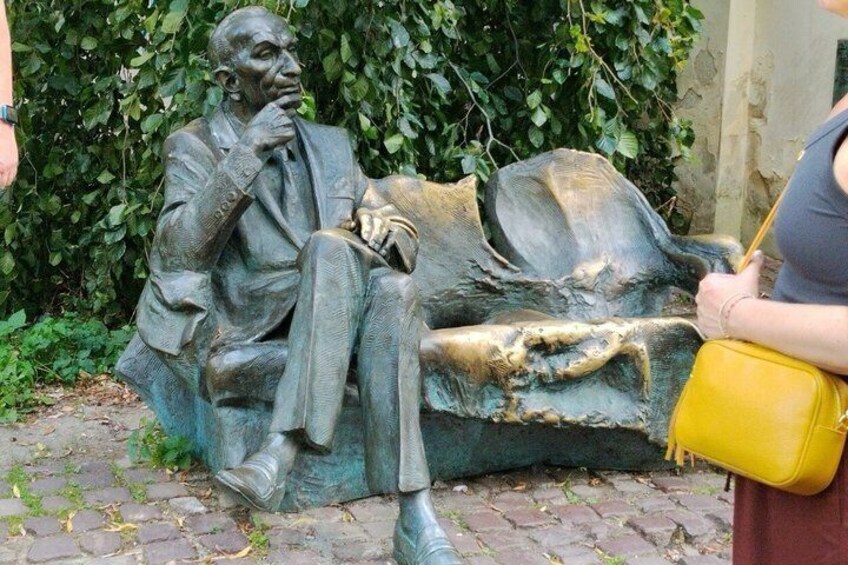 A bronze statue of a seated man with a thoughtful expression, wearing a suit and holding a cane. 5