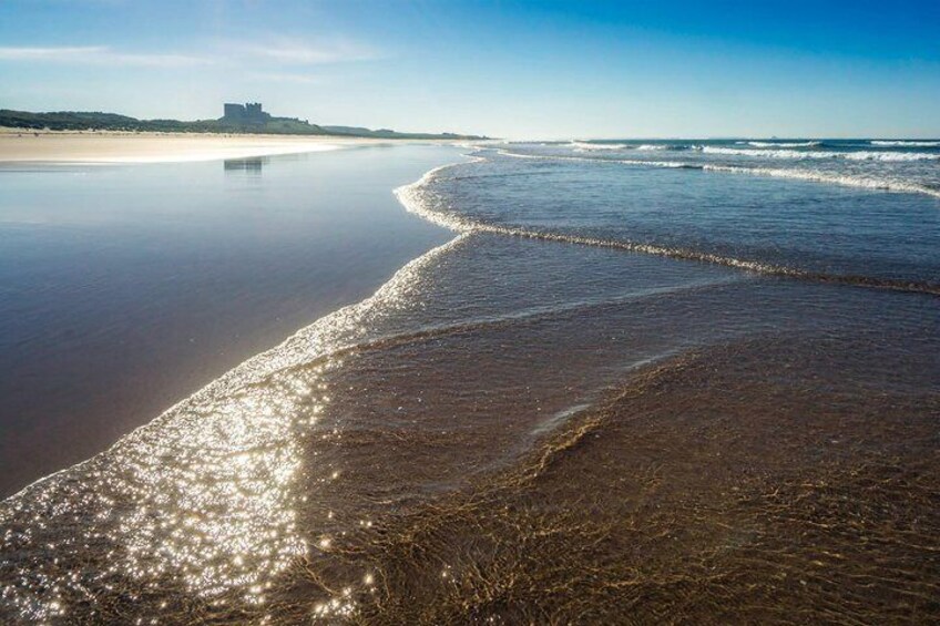 A beach with gentle waves, a clear sky, and a distant structure on the horizon. 2
