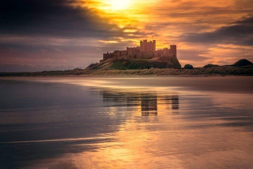 A castle on a hill overlooking a calm body of water with a sunset reflection. 1