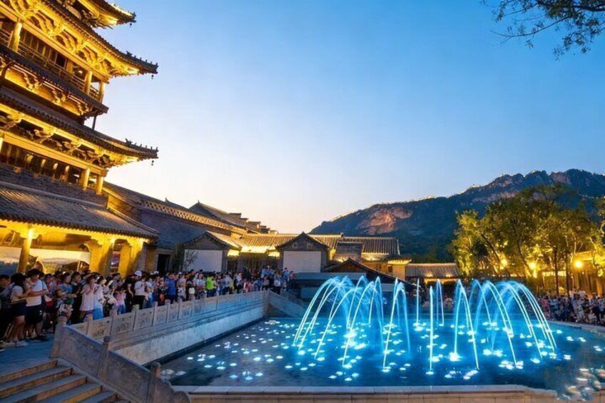 A traditional building with multiple tiers, a fountain with blue lights, and a mountainous backdrop. 2