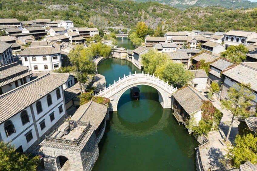 A traditional Chinese village with a stone bridge over a river, surrounded by white buildings with tiled roofs. 3