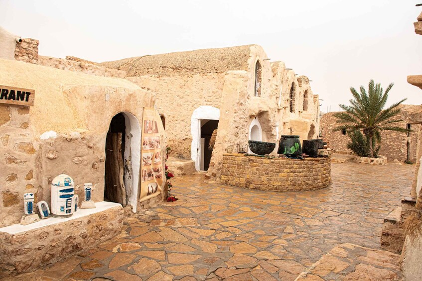 A stone-paved courtyard with traditional architecture, including arched doorways and a sign that reads 'TRANT.' 4