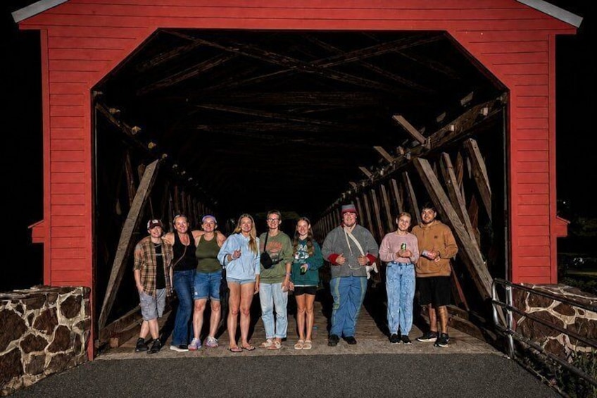 A group of people standing in front of a red covered bridge. 1