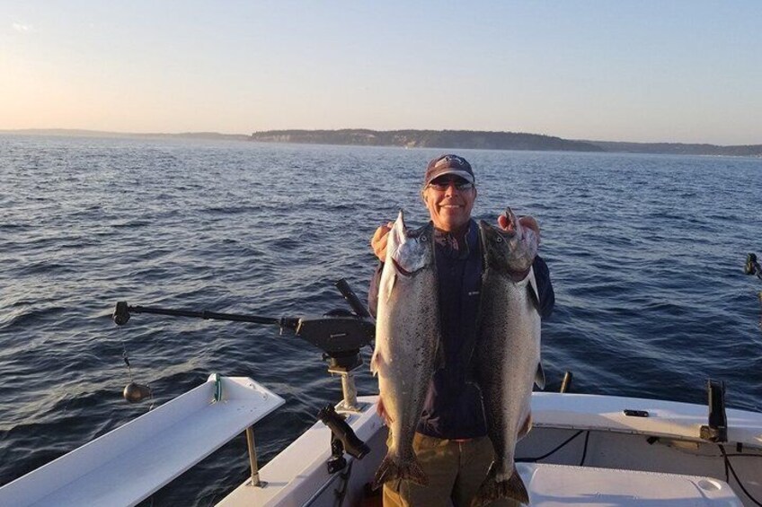 A person on a boat holding two fish. 1