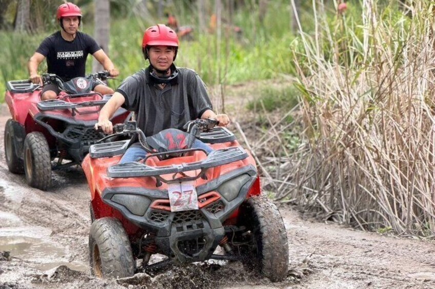 Two people riding ATVs on a muddy trail surrounded by vegetation. 4