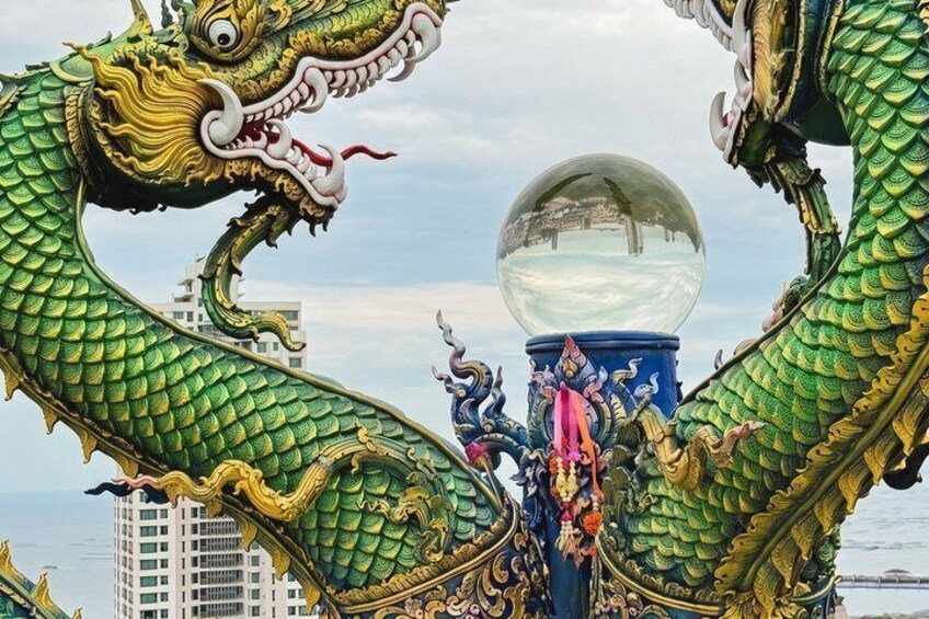 A large green dragon sculpture with a reflective sphere in the center, set against a cityscape. 2