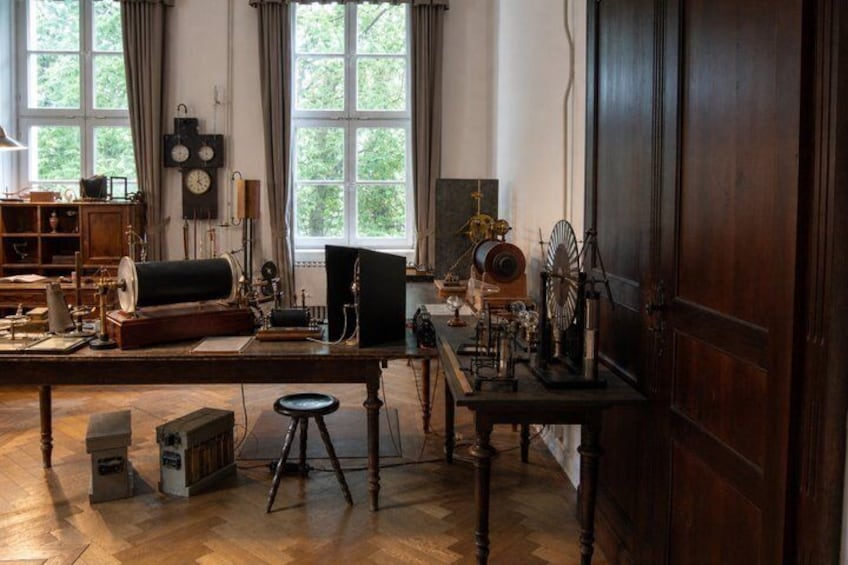 A room with wooden furniture, a desk with scientific instruments, a large window, and a door. 4