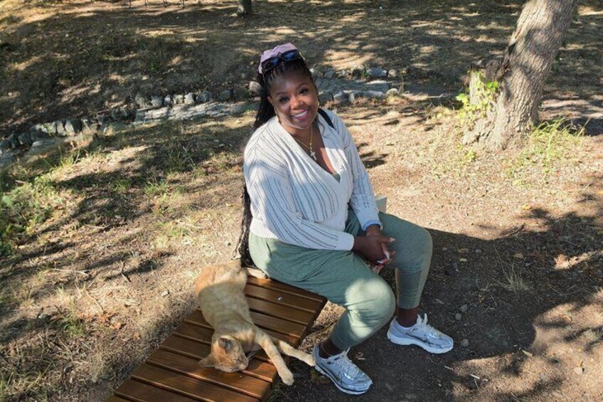 A person sitting on a wooden bench in a park with a dog lying beside them. 3