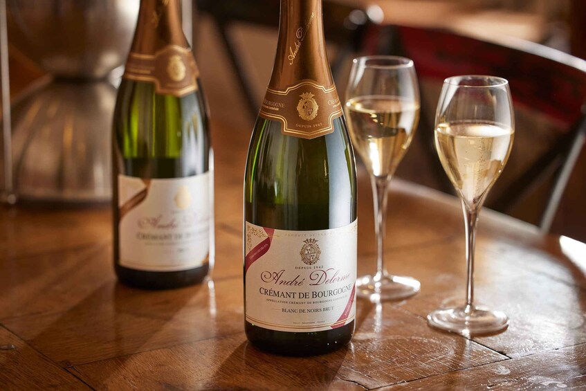 Two bottles of André Delorme Crémant de Bourgogne on a wooden table, with one glass partially filled with the wine. 1