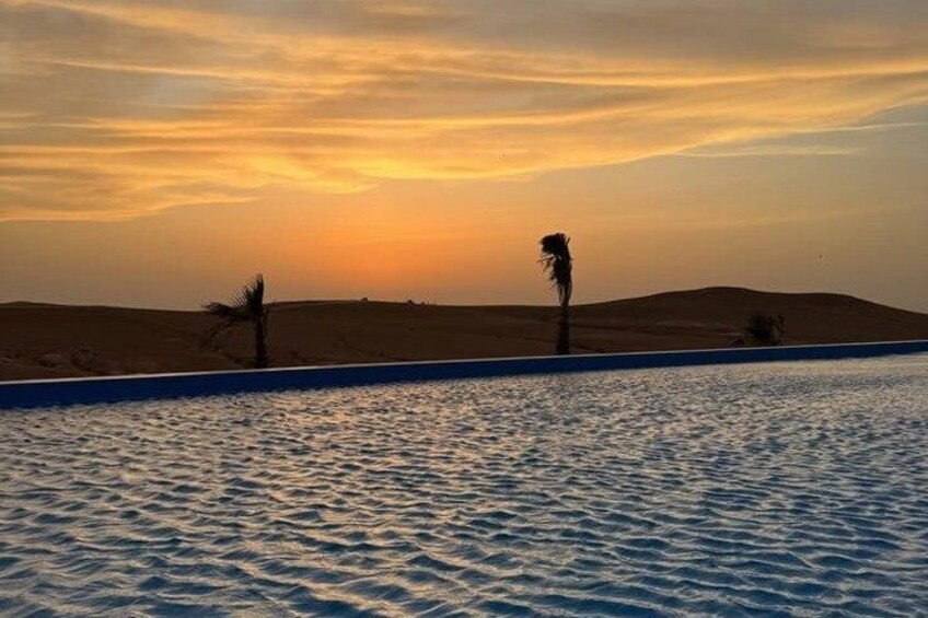 A desert landscape with a pool, palm trees, and a sunset. 2