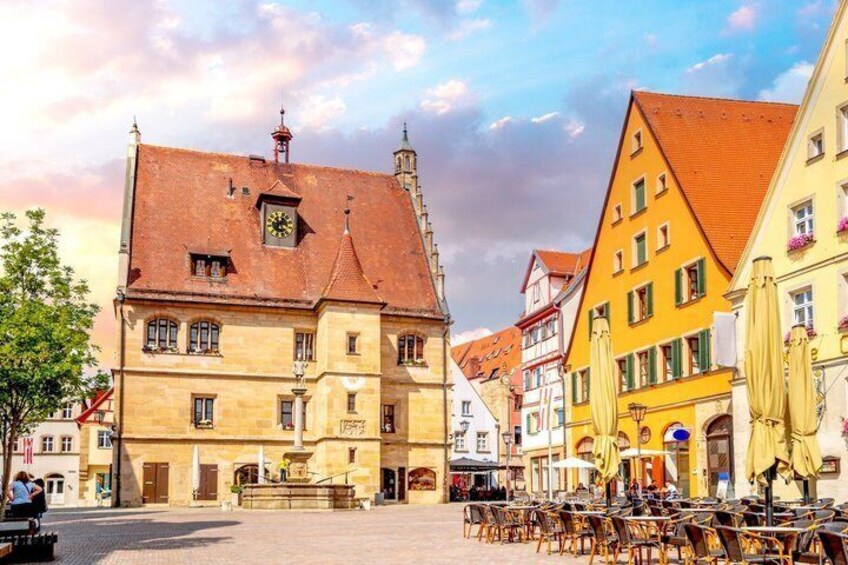 A European town square with historic buildings, outdoor seating, and a clock tower. 2