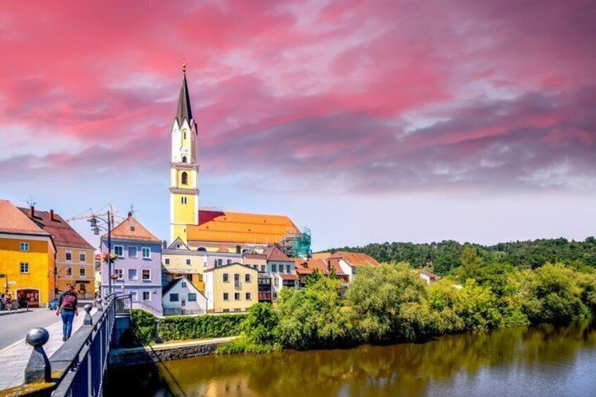 A town with a prominent church tower, colorful buildings, a river, and a bridge. 3